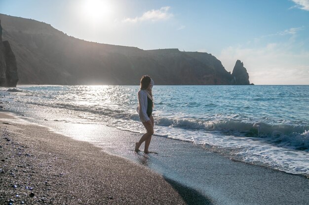 Enfoque selectivo feliz mujer sensual despreocupada con cabello largo en traje de baño negro posando en la playa al atardecer