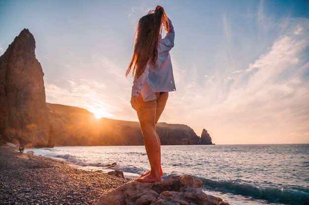 Enfoque selectivo feliz mujer sensual despreocupada con cabello largo en traje de baño negro posando en la playa al atardecer