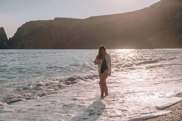 Enfoque selectivo feliz mujer sensual despreocupada con cabello largo en traje de baño negro posando en la playa al atardecer