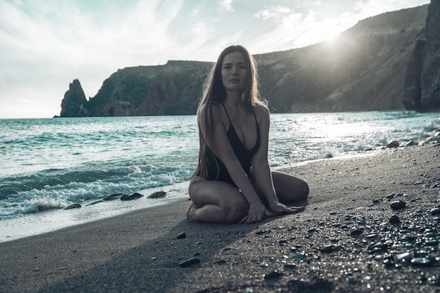 Enfoque selectivo feliz mujer sensual despreocupada con cabello largo en traje de baño negro posando en la playa al atardecer