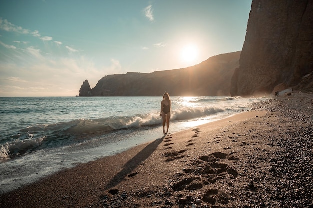 Enfoque selectivo feliz mujer sensual despreocupada con cabello largo en traje de baño negro posando en la playa al atardecer