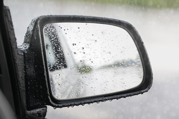 Enfoque selectivo de gotas de lluvia y reflejo en el espejo retrovisor lateral durante la lluvia fuerte. Muy poca profundidad de composición de campo.