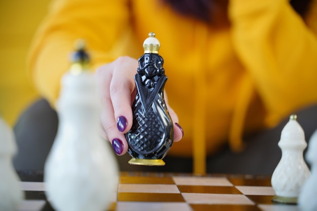 Enfoque selectivo del hermoso ajedrez en el tablero de ajedrez en la habitación Primer plano de la parte del cuerpo de una mujer irreconocible jugando en el juego de mesa