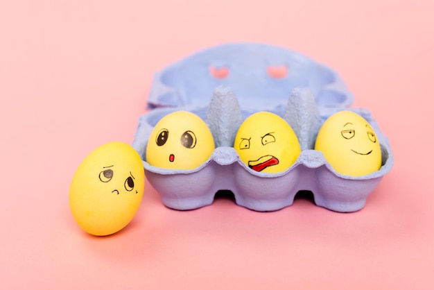 Enfoque selectivo de huevos de Pascua con expresiones faciales en bandeja de huevos sobre fondo rosa.