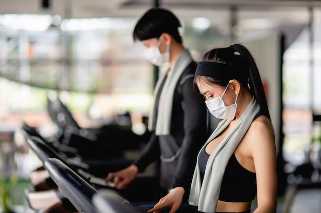 Enfoque selectivo, joven mujer sexy con ropa deportiva y reloj inteligente y joven borroso Están de pie programa de configuración en la cinta para hacer ejercicio en el gimnasio moderno, espacio de copia