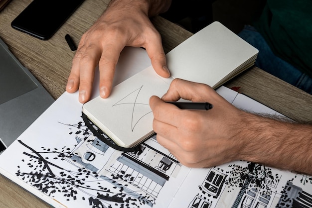 Foto enfoque selectivo de las manos del hombre dibujando en el cuaderno en la mesa de madera junto al álbum y los aparatos
