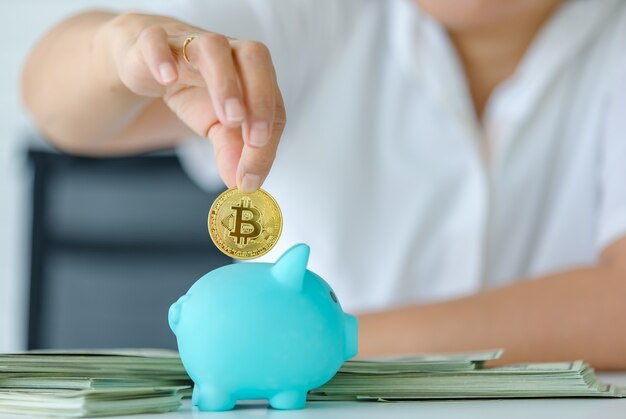 Enfoque selectivo en la moneda, una mano que sostiene el símbolo de dinero bitcoin y lo coloca en la caja de ahorro de alcancía. Concepto de tesoro de criptomonedas e inversión para el futuro.