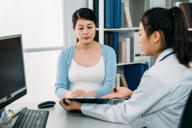 enfoque selectivo de una mujer embarazada japonesa escuchando a su médico ginecólogo explicando el diagnóstico con una mirada seria en el escritorio del hospital