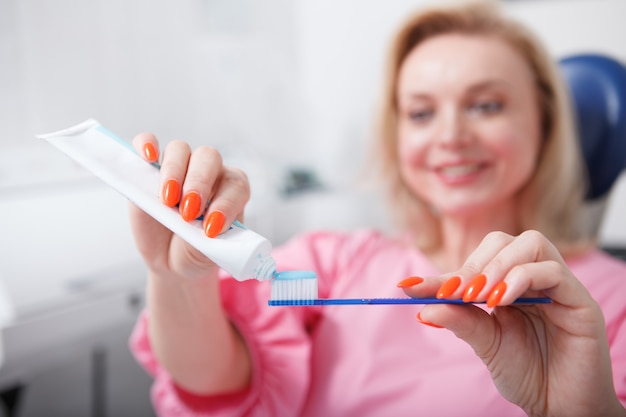 El enfoque selectivo en la mujer de pasta de dientes está apretando un cepillo de dientes