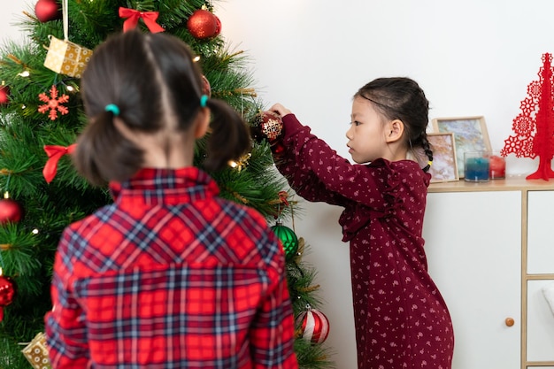 Enfoque selectivo Una niña china está decorando el árbol de Navidad con su hermana en la sala de estar de su casa.