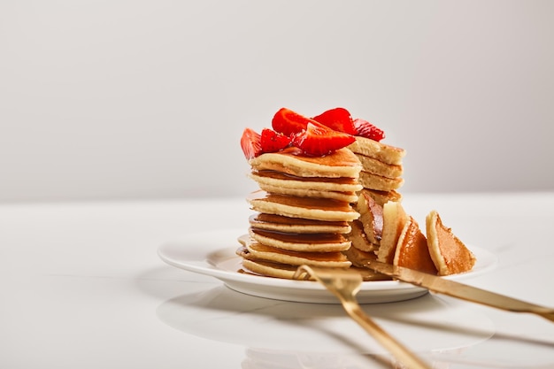 Enfoque selectivo de panqueques con fresas y cubiertos dorados en plato blanco aislado en gris