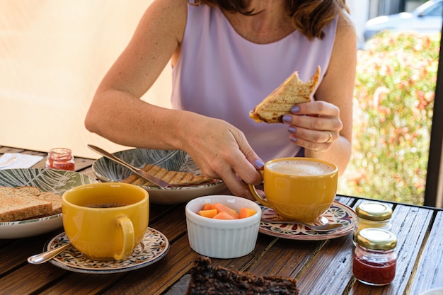 Enfoque selectivo. Porción de papaya rodeada de taza de café, pan integral, mermeladas variadas y mujer tomando una taza de café con leche.