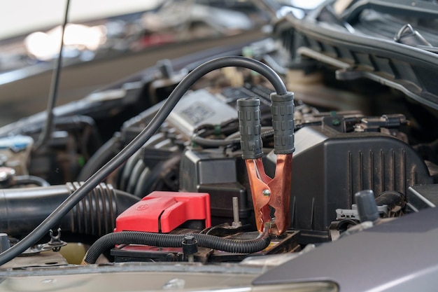 Enfoque selectivo de primer plano del mecánico que conecta los cables de puente a la batería de carga del automóvil