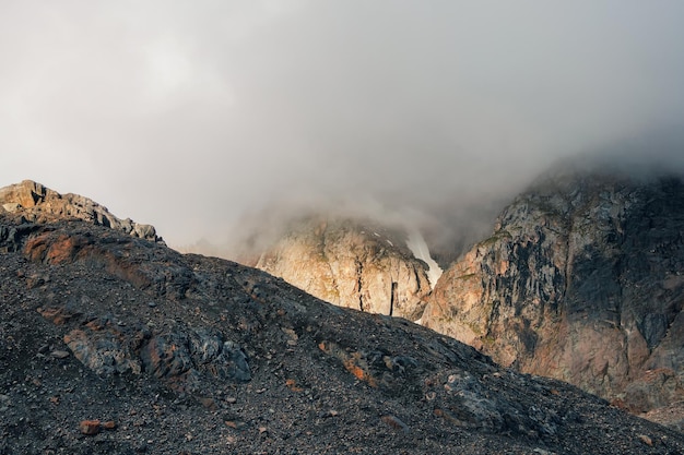 Enfoque suave Paisaje fantasmal atmosférico con siluetas borrosas de rocas doradas afiladas en nubes bajas Vista espectacular a grandes montañas borrosas en neblina de lluvia en nubes bajas grises