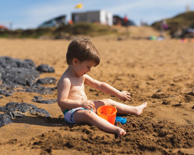 Enfoque superficial de un adorable niño jugando con sus juguetes en la playa.