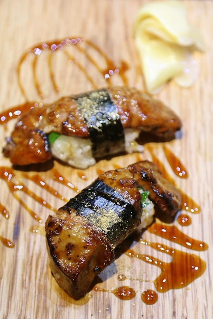 El enfoque superficial de primer plano del menú de sushi de foie gras de comida japonesa viene como un par cubierto con una salsa especial envuelta en algas Jengibre en escabeche colocado uno al lado del otro en un plato de madera fondo borroso