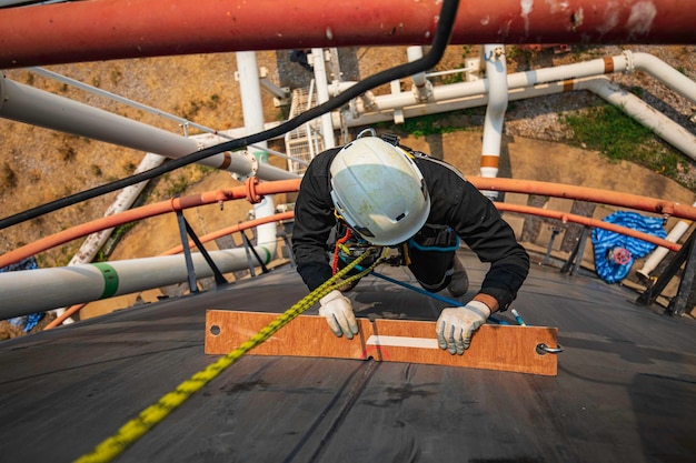 Enfoque vista superior trabajador masculino abajo altura techo del tanque acceso por cuerda inspección de seguridad del espesor del tanque de almacenamiento de petróleo crudo
