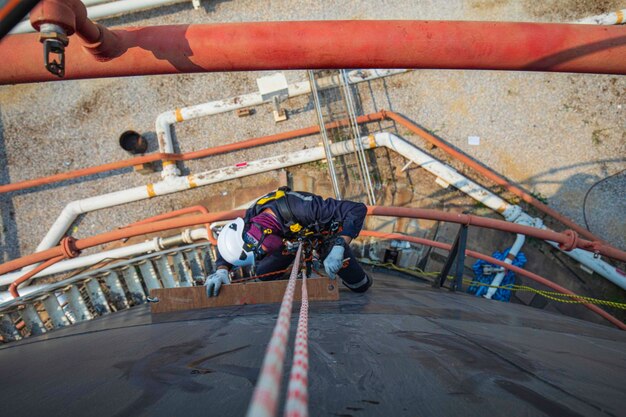 Enfoque vista superior trabajador masculino abajo altura techo del tanque acceso por cuerda inspección de seguridad del espesor del tanque de almacenamiento de petróleo crudo