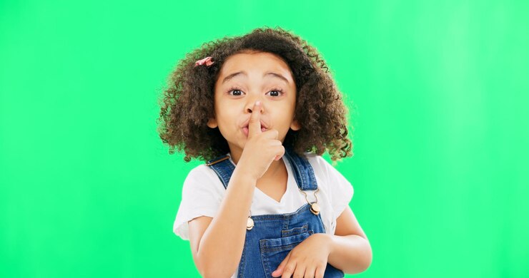 Foto enfrente a tela verde e a criança com o dedo nos lábios para silêncio silencioso ou gesto de silêncio no fundo do estúdio sussurro de ruído e retrato de menina com emoji secreto e símbolo de mão enquanto posa isolado