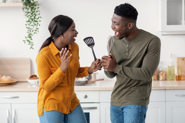 Engañando juntos a alegres cónyuges negros divirtiéndose en el interior de la cocina