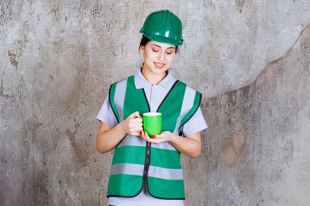 Engenheira com capacete verde segurando uma caneca de café verde