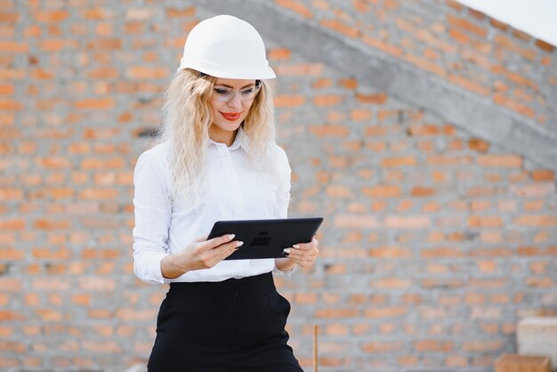 Engenheira de construção. Arquiteto com um computador tablet em uma construção. Jovem mulher olhando, construindo local de construção no fundo. Conceito de construção