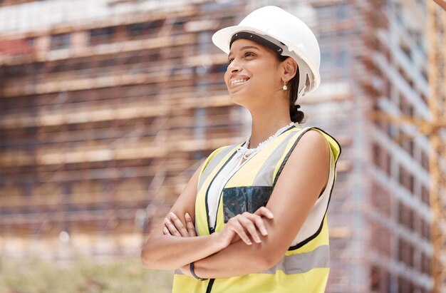 Engenheira de construção de braços cruzados e trabalhadora de construção pensante com objetivos de sorriso ou visão de arquitetura imobiliária Feliz desenvolvimento de engenharia de funcionários ou capacete no local de trabalho da propriedade