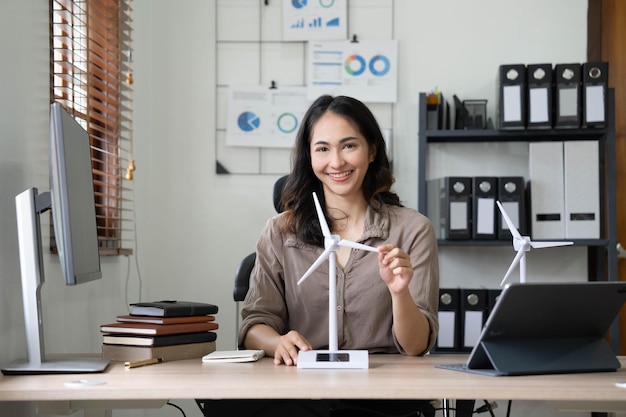 Engenheira de energia alternativa feminina segura um modelo de amostra de energia de moinho de vento e discute com colega sobre energia alternativa no escritório