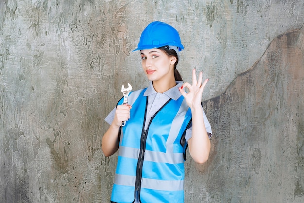 Engenheira de uniforme azul e capacete segurando uma chave metálica.