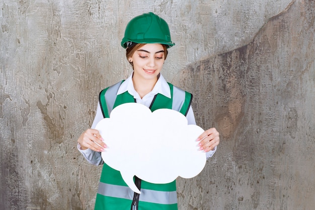 Engenheira de uniforme verde e capacete segurando um quadro de informações em forma de nuvem