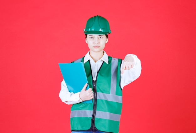 Engenheira de uniforme verde segurando uma pasta azul e ligando para o colega