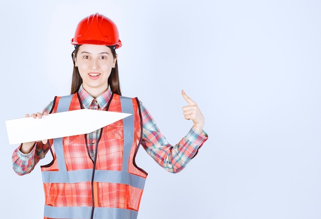 Engenheira em capacete vermelho, segurando uma seta apontando para a direita.