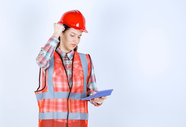 Engenheira no capacete vermelho, trabalhando na calculadora e parece confusa ou emocionada.