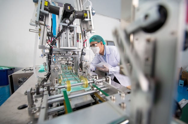 Engenheiro adulto médio examinando a peça da máquina em uma linha de produção em uma fábrica.