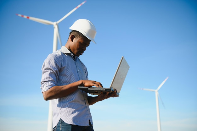 Engenheiro africano em pé e hoding laptop com turbina eólica