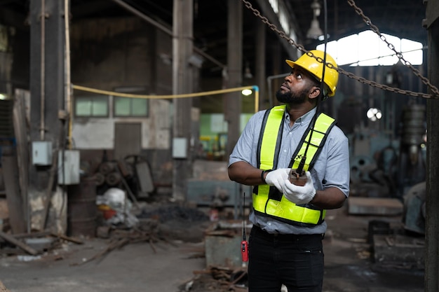 Engenheiro afro-americano operando guindaste aéreo de controle para mover metais pesados na fábrica