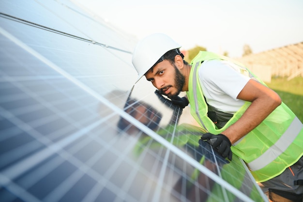 Engenheiro árabe de capacete e macacão castanho verificando a resistência em painéis solares ao ar livre homem indiano trabalhando na estação