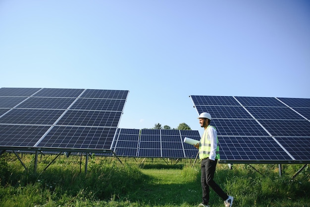 Engenheiro árabe de pé no campo com fileiras de painéis solares