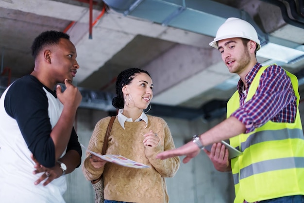 engenheiro arquiteto usando computador tablet enquanto mostra planos de design de casa para um jovem casal multiétnico no canteiro de obras