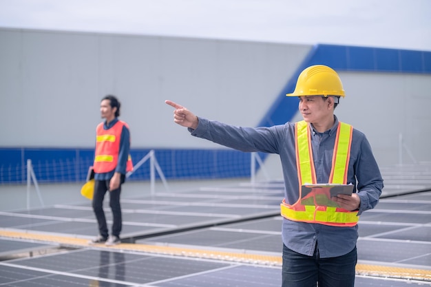 Engenheiro Asiático de pé na fábrica de telhado e verificando a energia da célula solar de energia solar pela tecnologia de tablet