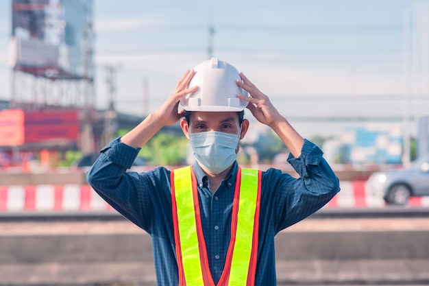 Engenheiro asiático em pé ao ar livre na construção do local postando construção de engenheiro confiante
