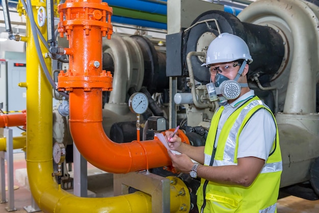 Engenheiro asiático usando óculos trabalhando na manutenção da sala da caldeira verificando dados técnicos do equipamento do sistema de aquecimentoTailândia usando máscara de gás