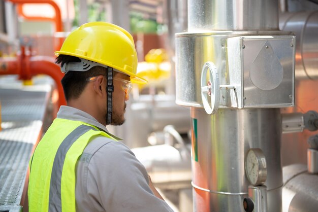 Engenheiro asiático usando óculos trabalhando na manutenção da sala da caldeira verificando dados técnicos do equipamento do sistema de aquecimentoTailândia