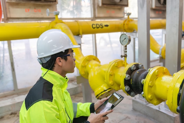 Engenheiro asiático usando óculos trabalhando na manutenção da sala da caldeira verificando dados técnicos do equipamento do sistema de aquecimentoTailândia