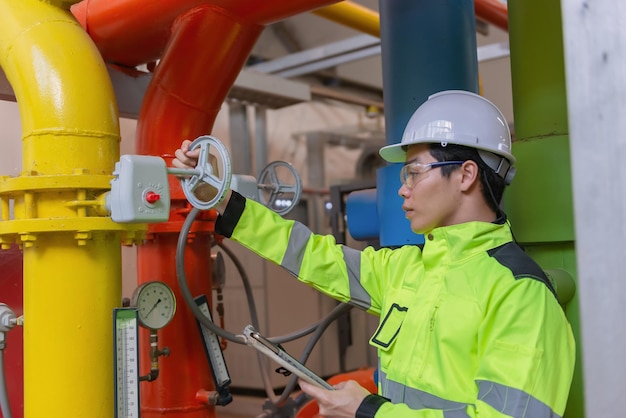 Engenheiro asiático usando óculos trabalhando na manutenção da sala da caldeira verificando dados técnicos do equipamento do sistema de aquecimentoTailândia