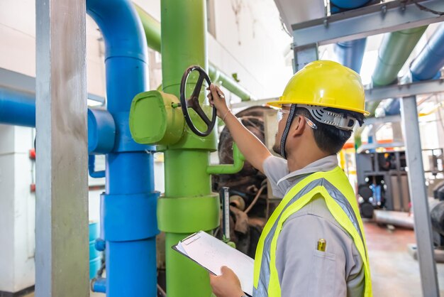 Engenheiro asiático usando óculos trabalhando na manutenção da sala da caldeira verificando dados técnicos do equipamento do sistema de aquecimentoTailândia