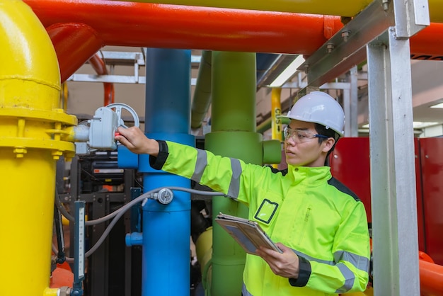 Engenheiro asiático usando óculos trabalhando na manutenção da sala da caldeira verificando dados técnicos do equipamento do sistema de aquecimentoTailândia