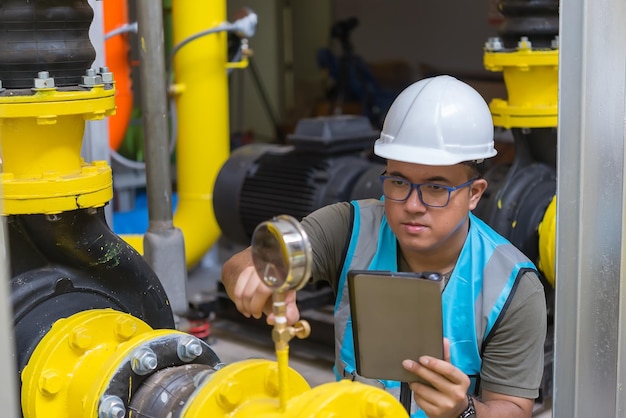 Engenheiro asiático usando óculos trabalhando na manutenção da sala da caldeira verificando dados técnicos do equipamento do sistema de aquecimentoTailândia