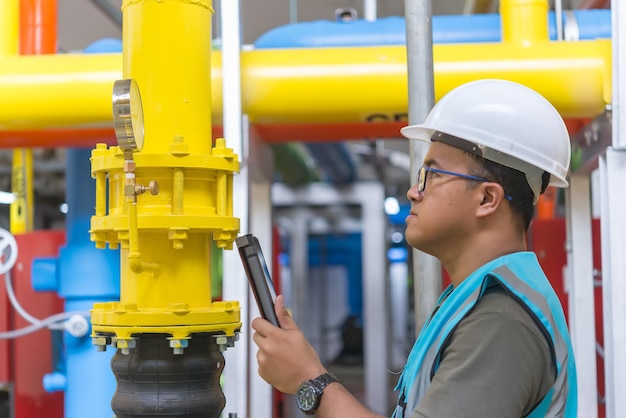 Engenheiro asiático usando óculos trabalhando na manutenção da sala da caldeira verificando dados técnicos do equipamento do sistema de aquecimentoTailândia