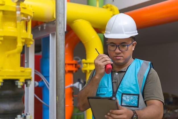 Engenheiro asiático usando óculos trabalhando na manutenção da sala da caldeira verificando dados técnicos do equipamento do sistema de aquecimentotailândia